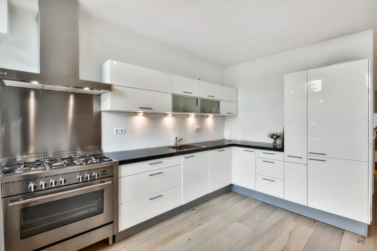house-cleaning-img-1 Modern white kitchen with stainless steel stove and hood, black countertop, and tall white cabinets.