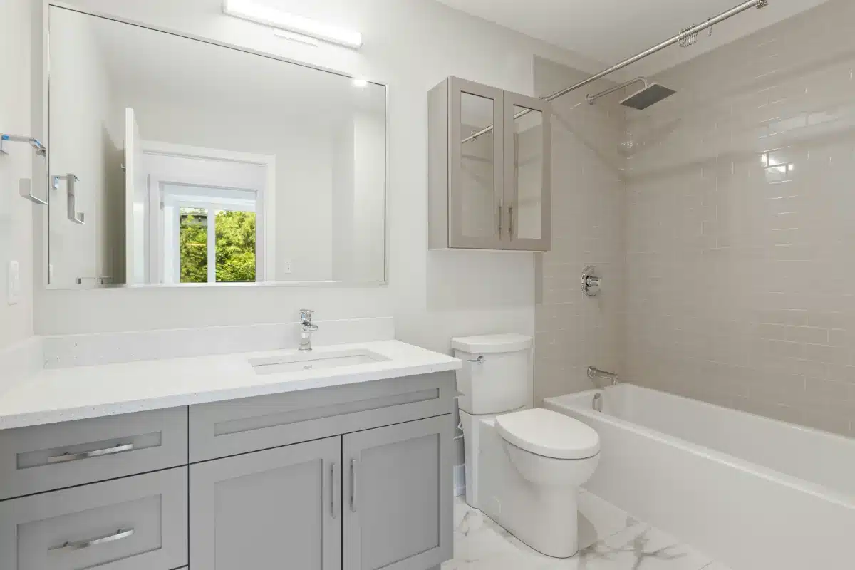 house-cleaning-img-2 Modern bathroom with gray vanity, white countertop, toilet, and a tiled tub/shower area with chrome fixtures