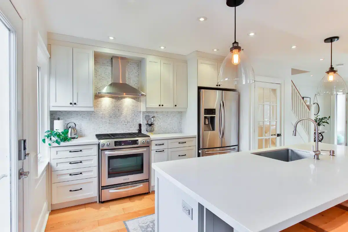 real-estate-cleaning-img-2 Bright modern kitchen with white cabinets, stainless steel fridge and range, and a large white island with a sink and pendant lights above.